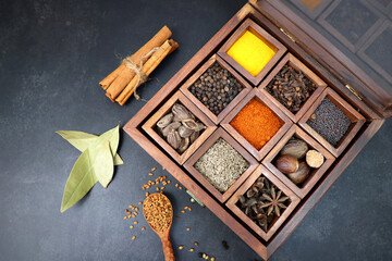 Variety of Indian spices and herbs in a wooden box. Multicolored spices in a wooden organizer, top view. Seasoning background. Bay Leaf, Black Pepper, Cinnamon, Cloves, Coriander, Turmeric, red chili. - obrazy, fototapety, plakaty