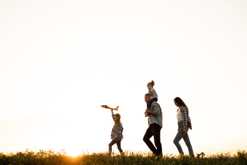 family of tourists walking at sunset across the field in summer silhouettes of dad mom and daughters. People walking on the horizon. Parents with children travel light. Happy family concept.