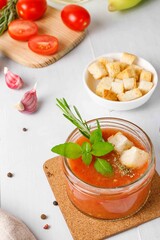 Cold gazpacho soup in a small jar,served with basil and croutons. Close-up on a light wooden background, vertical