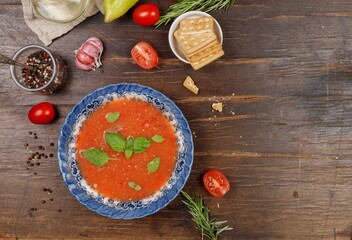 Gazpacho, or tomato soup in a vintage blue plate, on a rough wooden table, with crackers, peppers and tomatoes. Top view, copy of the space