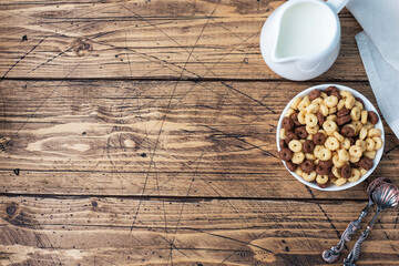Dry breakfast cereals. Chocolate and corn rings made from natural cereals with milk in a plate. Wooden rustic background, copy space.