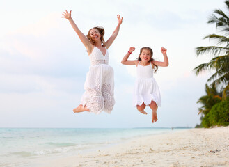 Optimistic mother and daughter jumping on beach