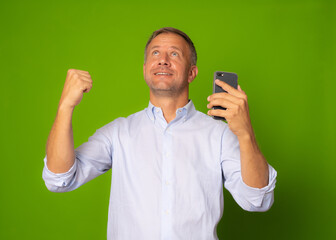Happy man holding smartphone and celebrating his success over green background