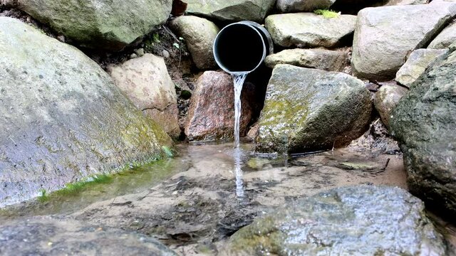 A stream of rainwater flows from a gray plastic pipe that is installed between the stones