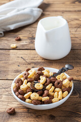 Dry breakfast cereals. Chocolate and corn rings made from natural cereals with milk in a plate. Wooden rustic background, copy space.