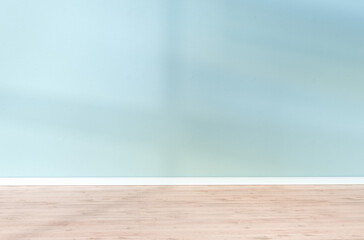 Light blue textured wall and wooden floor in empty room for displaying your product, light coming through window.