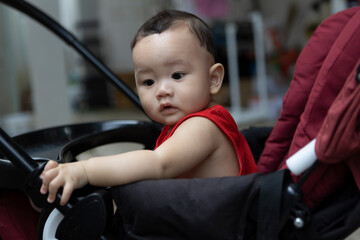 Cute 8 month old boy wearing a red shirt sitting on a red and black stroller