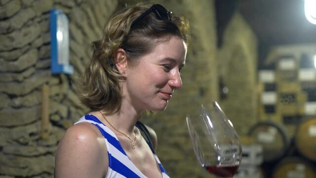 Portrait of a woman sommelier who tasting a flavor and checking quality of a red wine poured in transparent glass in a wine cellar. Wine Making concept . Image of happy and funny girl.