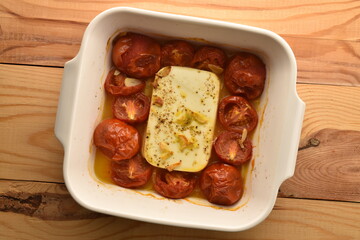 Feta cheese with cocktail tomatoes and spices in a white ceramic bowl, baked in the oven, top view.