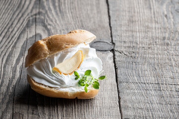 Shu cake profiteroles with whipped cream and lemon balm on wooden table