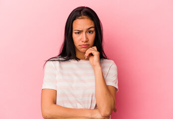 Young Venezuelan woman isolated on pink background suspicious, uncertain, examining you.