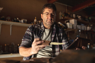 Caucasian male knife maker standing at desk, preparing knife in workshop