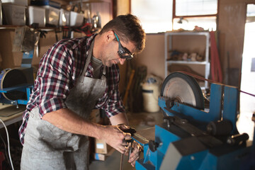 Caucasian male knife maker wearing apron and glasses , making knife in workshop
