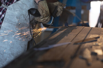 Hands of caucasian male knife maker wearing apron, using angle grinder in workshop
