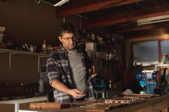 Caucasian male knife maker standing at desk, preparing knife in workshop