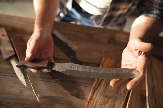 Hands of caucasian male knife maker in workshop, holding handmade knife