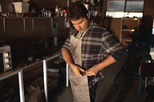 Caucasian male knife maker putting on apron in workshop