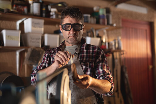 Caucasian male knife maker wearing apron and glasses , making knife in workshop