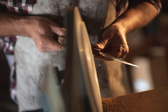 Hands of caucasian male knife maker wearing apron, making knife in workshop
