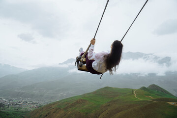 Dark hair girl ride on a swing in ossetia mountains