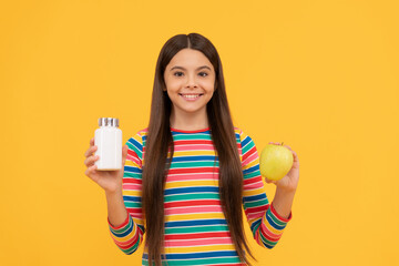 Happy kid hold apple fruit and medicine bottle yellow background, supplement