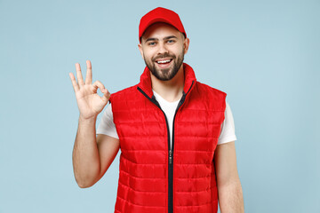 Professional happy delivery guy employee man in red cap white T-shirt vest uniform workwear work as dealer courier show ok okay gesture isolated on pastel blue color background studio Service concept