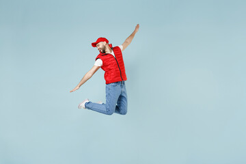 Obraz premium Full size body length side view delivery guy employee man in red cap white T-shirt vest uniform work dealer courier jump run go walk isolated on pastel blue color background studio. Service concept
