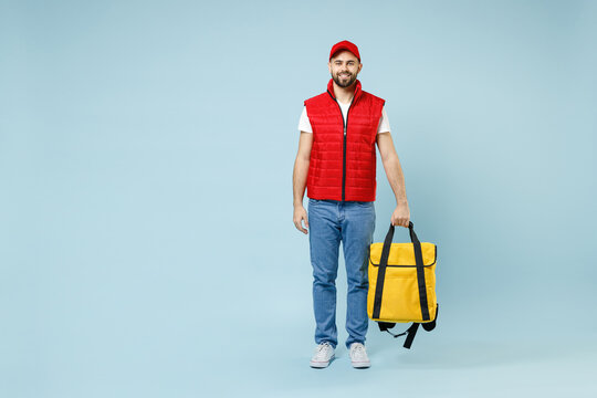 Full Size Body Length Delivery Guy Employee Man In Red Cap White T-shirt Uniform Work As Courier Hold Yellow Thermal Food Bag Backpack Isolated On Pastel Blue Color Background Studio. Service Concept.