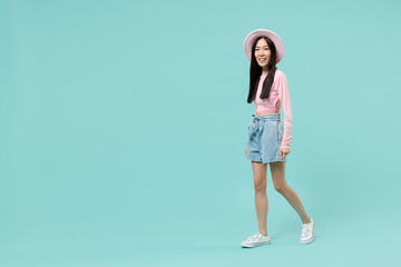 Full size body length smiling beautiful amazing marvelous young brunette asian woman 20s wears pink clothes walk moving strolling look camera isolated on pastel blue color background studio portrait