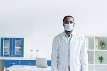 Fototapeta na wymiar African american scientist in medical mask and white coat looking at camera