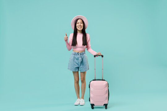 Full size body traveler tourist asian woman wear pink casual clothes hat hold suitcase bag isolated on pastel pink color background studio. Passenger travel abroad getaway. Air flight journey concept.