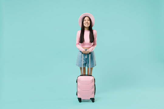 Full size body traveler tourist asian woman wear pink casual clothes hat hold suitcase bag isolated on pastel pink color background studio. Passenger travel abroad getaway. Air flight journey concept.