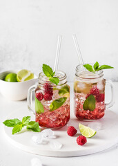Fototapeta na wymiar Two glass mason jars of cold summer refreshing mojito cocktail with raspberries, mint and lime. Selective focus. Copy space.