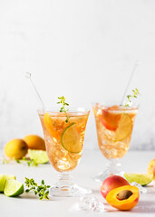Two glasses of fresh apricot cocktail with ice, lime and lemon thyme. Refreshing, homemade non-alcoholic cocktails in summer. Selective focus. Copy space.