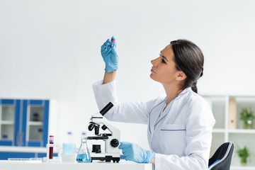 Side view of scientist in white coat looking at test tube near medical equipment