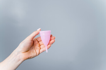 Close-up of a female hand with a pink menstrual cup on a white background. Caring for the environment. Eco friendly female intimate hygiene product. Copy space