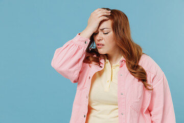 Young redhead chubby overweight woman 30s with curly hair in pink shirt put hand on face facepalm epic fail mistaken omg gesture isolated on pastel blue background studio. People lifestyle concept - obrazy, fototapety, plakaty