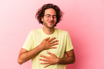 Young caucasian man isolated on pink bakcground laughs happily and has fun keeping hands on stomach.
