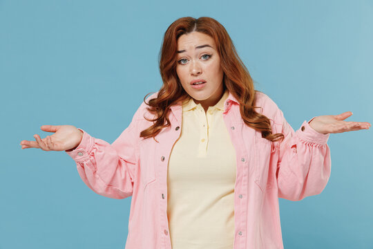 Young confused uncertain doubtful redhead chubby overweight woman 30s wearing pink shirt casual clothes spread hands screaming shout isolated on pastel blue background studio People lifestyle concept.