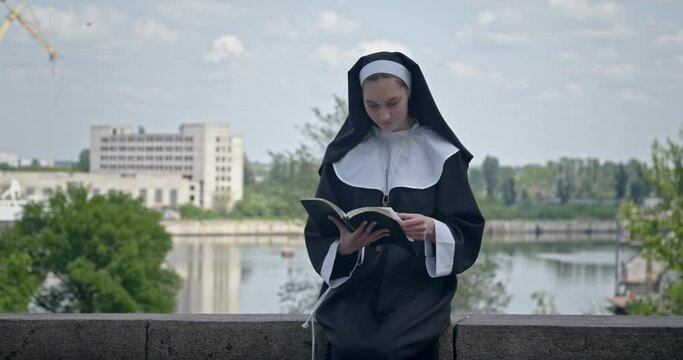 Young nun reading Bible outdoors