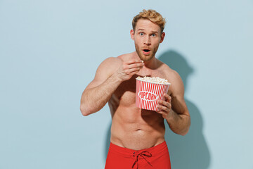 Handsome young surprised sexy man in red shorts swimsuit relax near hotel pool hold popcorn...