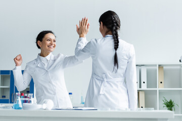 Happy african american scientist showing yes gesture and giving high five to colleague in lab
