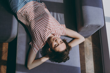 Fototapeta premium Top view from above young woman in casual clothes lying on grey sofa hold hands behind head neck relax take nap during day break on weekends rest indoors flat at home People lifestyle leisure concept