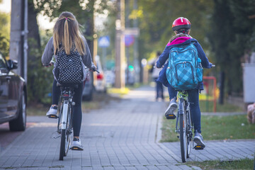 Two school girls riding bicycles on the sidewalk