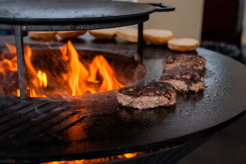 Process of grilling fresh meat cutlets for burgers on brazier with hot flame at summer local food market - close up view. Outdoor cooking, gastronomy, cookery, street food concept
