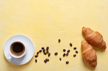 A cup of fresh coffee and croissants on a yellow background with copy space