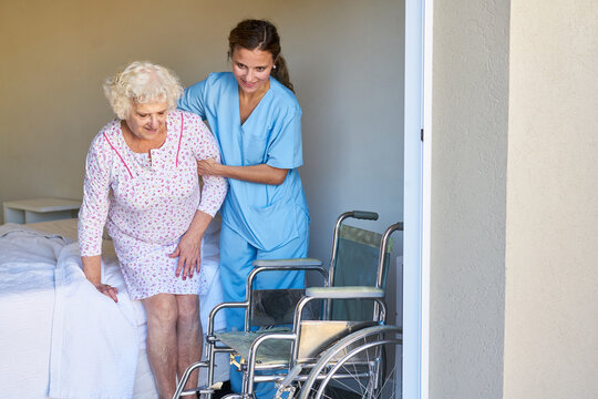 Pflegehilfe hilft Seniorin beim Aufstehen im Pflegeheim