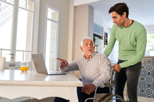 Junger Mann hilft Senior im Rollstuhl am Laptop Computer