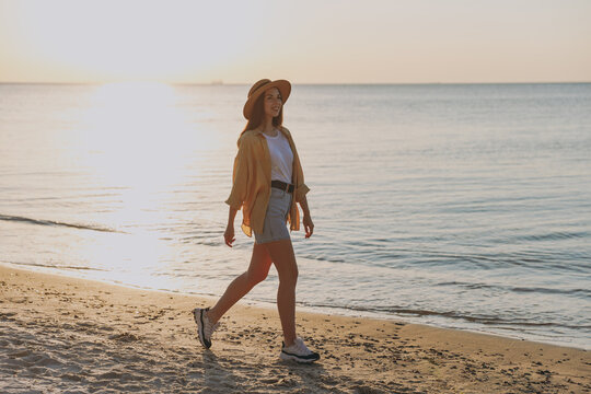 Side profile view fun young woman 20s wearing straw hat shirt summer casual clothes stand resting walking outdoors at sunrise sun dawn over sea background. People vacation lifestyle journey concept