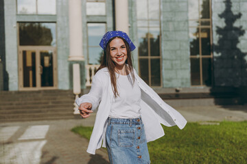 Smiling satisfied young excited student woman 20s wear in blue bandana shirt summer casual clothes rest standing in front of city building walk in town centre outdoors People urban lifestyle concept.